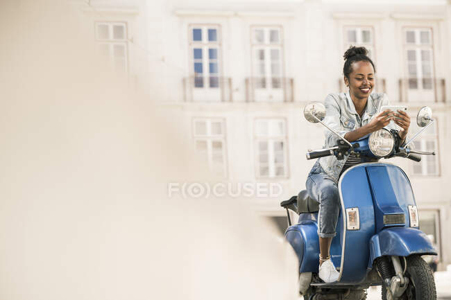 Smiling young woman with motor scooter and mobile phone in the city, Lisbon, Portugal — Adults, break - Photo |