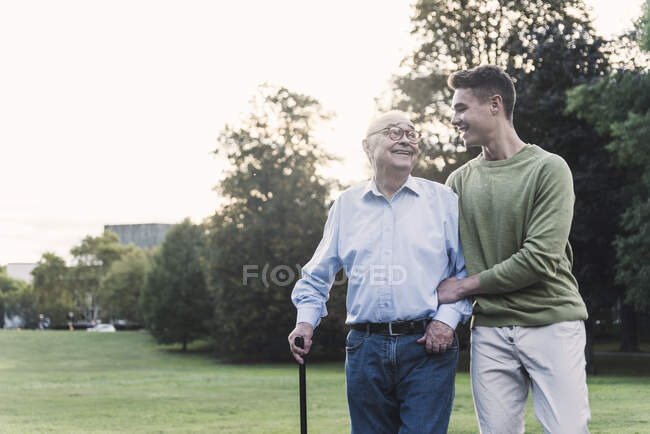 Молодой человек помогает дедушке гулять в парке — стоковое фото