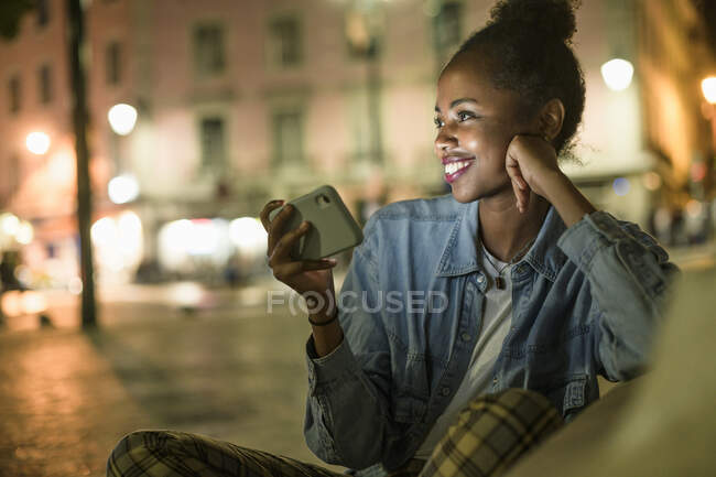 Portrait of happy young woman with smartphone in the city by night, Lisbon, Portugal — Stock Photo