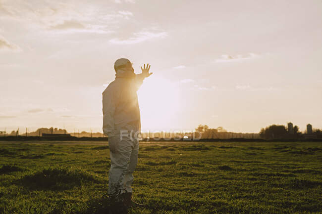 Hombre con traje protector y máscara en el campo al atardecer - foto de stock