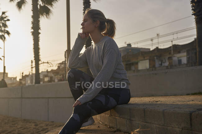 Sportliche junge Frau macht Pause an der Strandpromenade bei Sonnenuntergang — Stockfoto