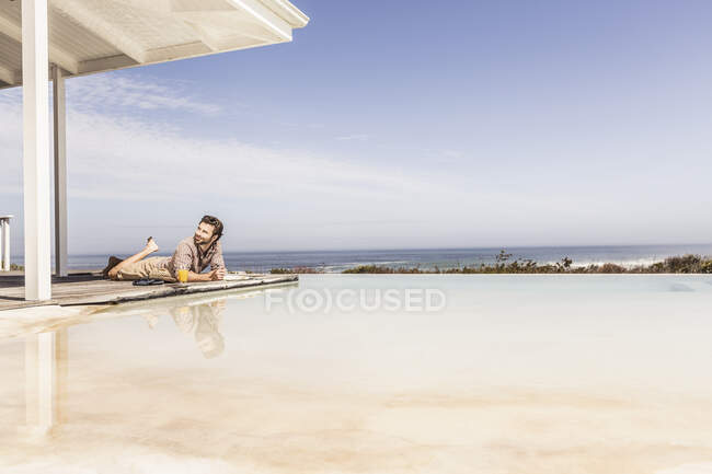 Uomo sdraiato accanto alla piscina in una casa al mare — Foto stock