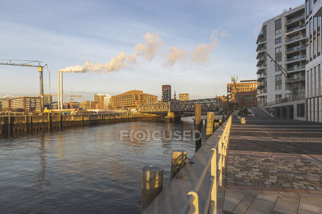 Alemania, Hamburgo, HafenCity puerto al amanecer con humo saliendo de chimeneas industriales en el fondo - foto de stock
