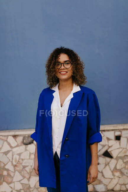 Portrait of smiling woman wearing glasses and blue blazer, blue wall in the background — Foto stock