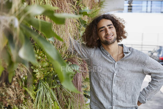 Porträt eines lächelnden jungen Mannes vor einer Pflanzenmauer — Stockfoto