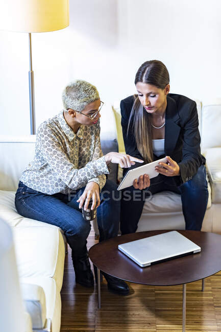 Two businesswomen working together in lounge sharing tablet — Stock Photo