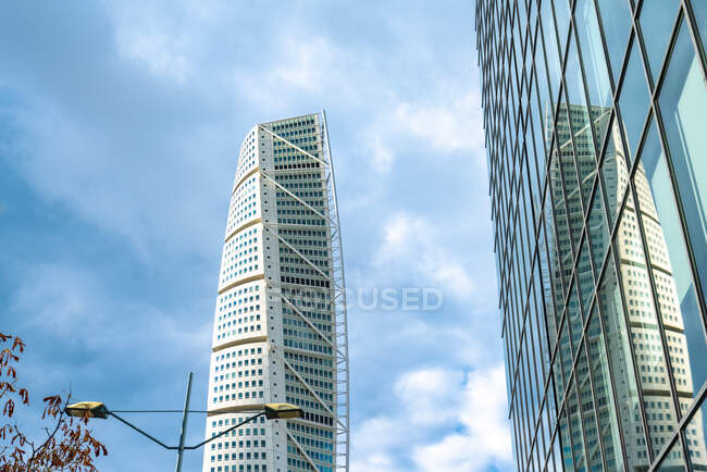 Vista de ángulo bajo de la torre del torso giratorio que refleja en el edificio de vidrio contra el cielo - foto de stock