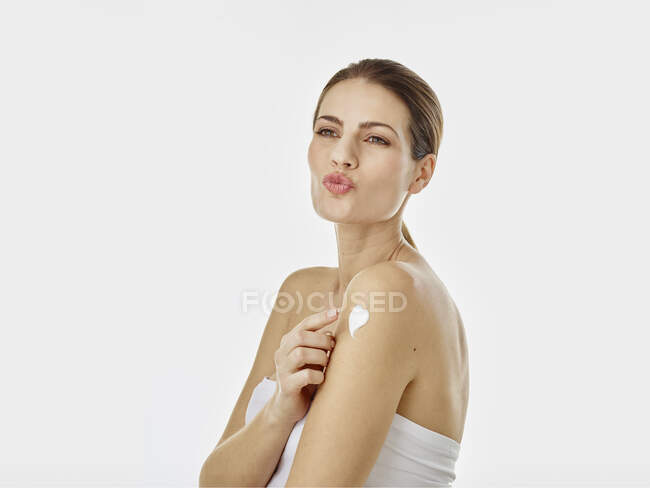 Retrato de la mujer haciendo pucheros en la boca aplicando crema corporal en su brazo - foto de stock