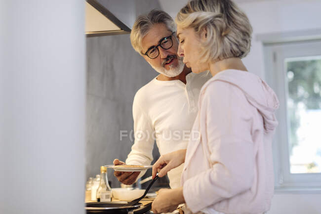 Casal maduro preparando panquecas na cozinha em casa — Fotografia de Stock