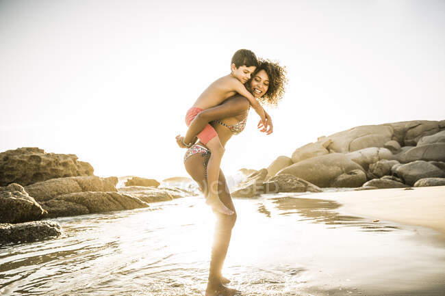 Mãe feliz carregando seu filho piggyback na praia — Fotografia de Stock