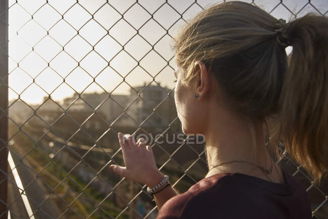 Jeune femme sportive regardant à travers une clôture — Photo de stock