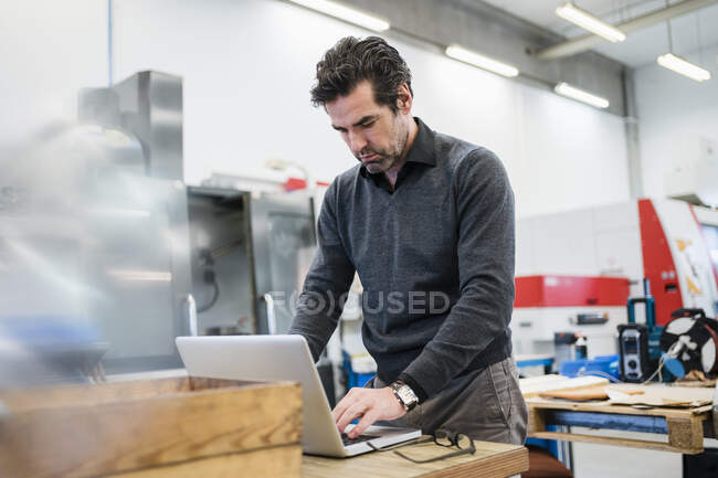 Empresario usando portátil en una fábrica - foto de stock