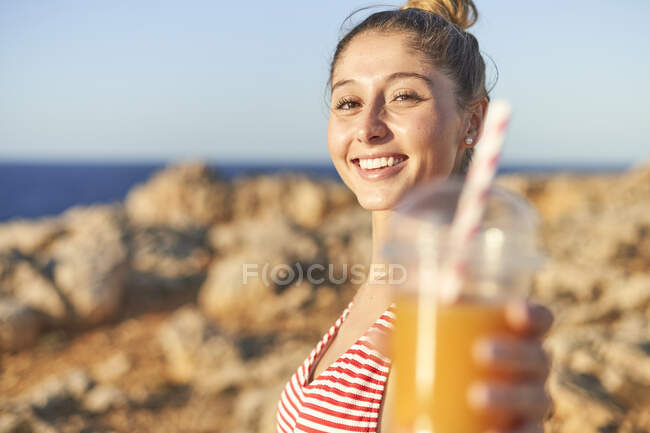 Jovem mulher bebendo suco na praia rochosa — Fotografia de Stock