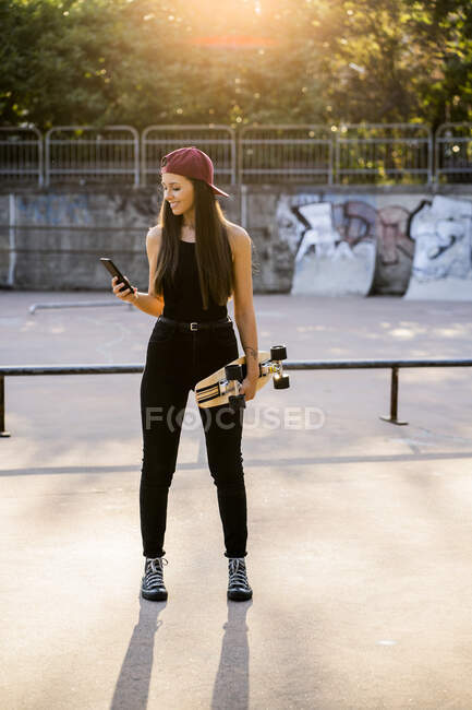 Young woman with smartphone and skateboard at skatepark — Stock Photo