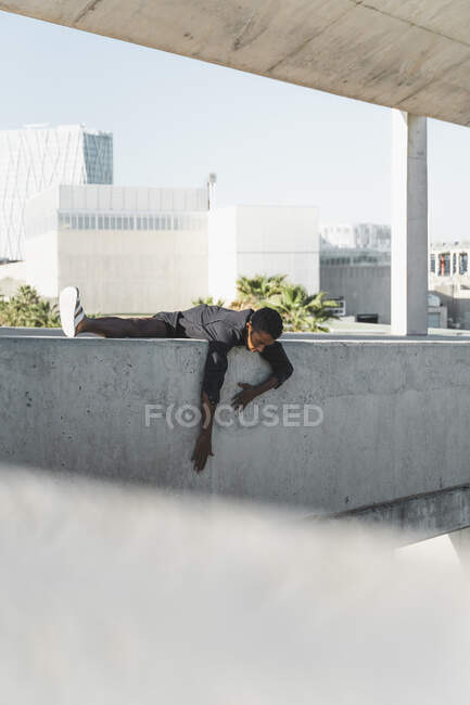 Young man wearing black kaftan climbing on a concrete wall — Stock Photo