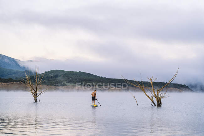 Uomo stand up paddle surf su un lago nella nebbia — Foto stock