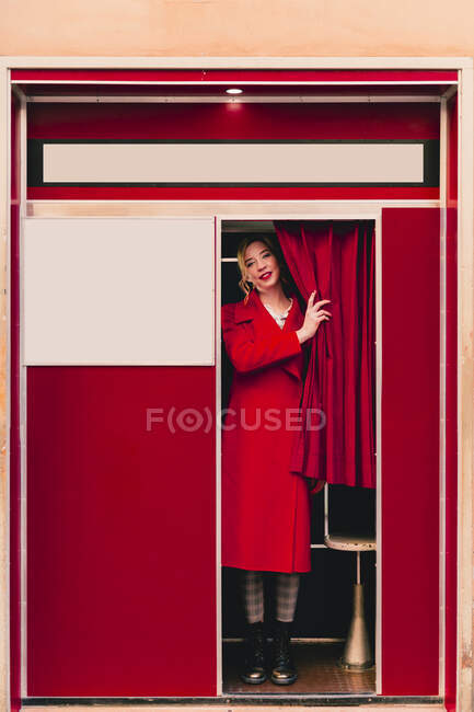 Ritratto di giovane donna vestita di rosso in piedi in una cabina fotografica — Foto stock