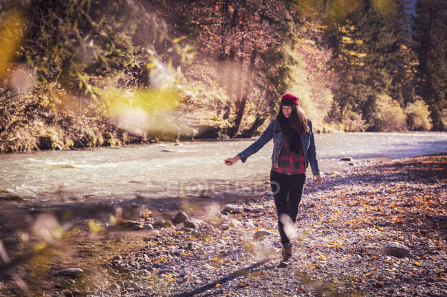 Woman wearing red woolly hat and denim jacket walking at riverside in autumn — Stock Photo