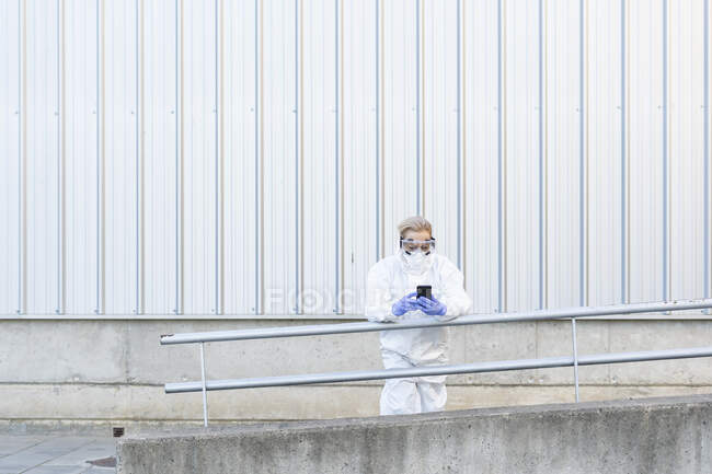 Female scientist wearing protective suit and mask and using smartphone — Stock Photo