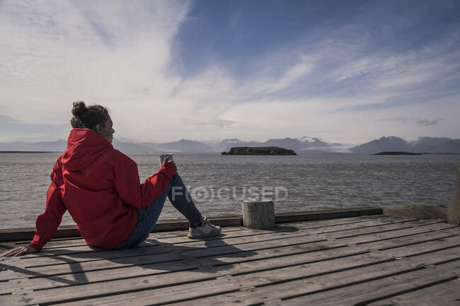 Jovem mulher sentada em um molhe, olhando para o mar, Sudeste da Islândia — Fotografia de Stock