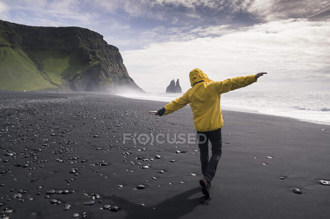 Uomo maturo che cammina su una spiaggia di lava in Islanda, con le braccia tese — Foto stock