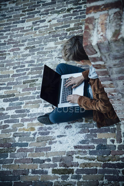 Мбаппе использует ноутбук и сидит на каменном полу в городе — стоковое фото