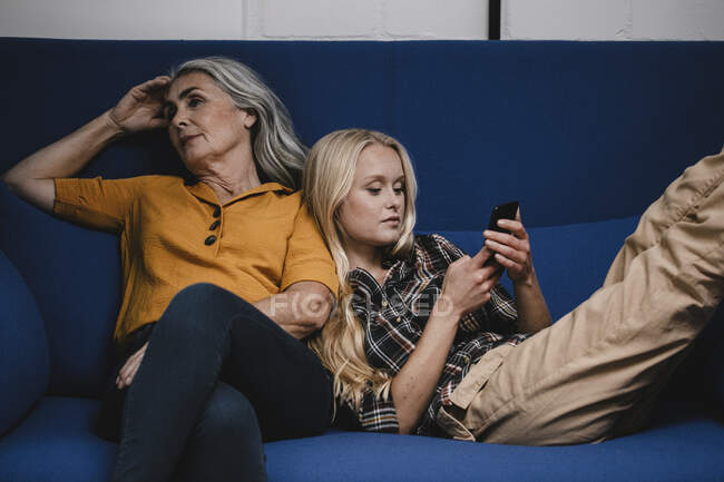 Donna utilizzando smartphone sul divano accanto a sua madre — Foto stock