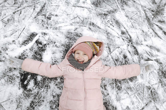 Portrait of happy girl with arms outstretched lying on ice — Stock Photo