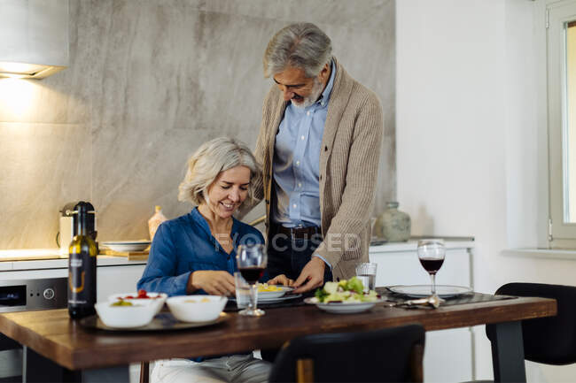 Reifer Mann serviert seiner Frau zu Hause Abendessen in der Küche — Stockfoto