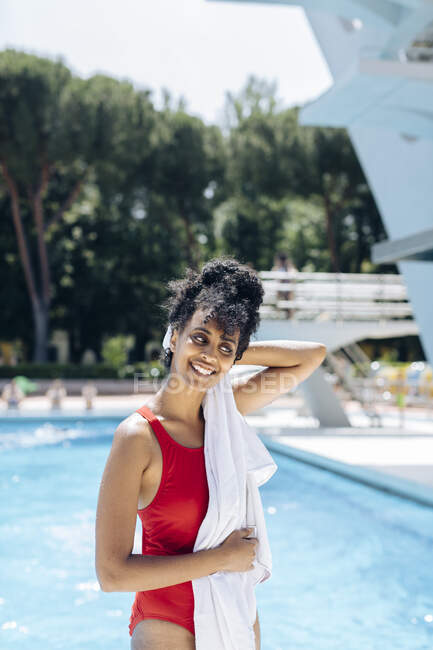 Retrato de una joven sonriente en traje de baño rojo toallando frente a una piscina - foto de stock