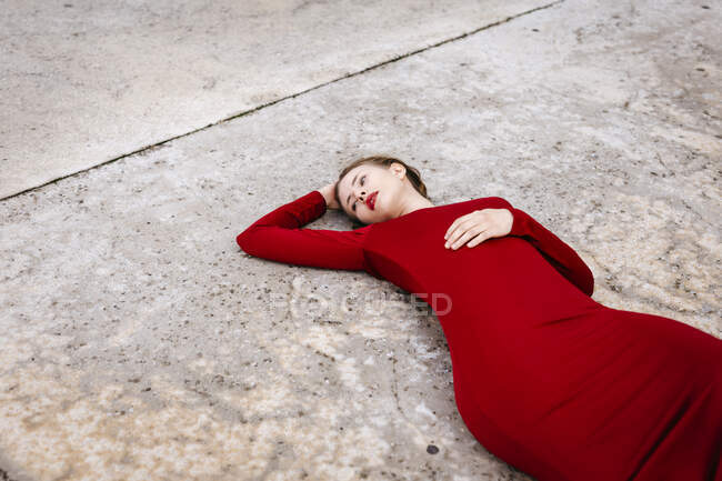 Portrait of young woman wearing red dress lying on ground outdoors — Stock Photo