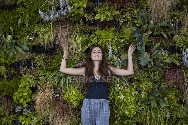 Portrait of smiling young woman with closed eyes in front of plant wall — Stock Photo