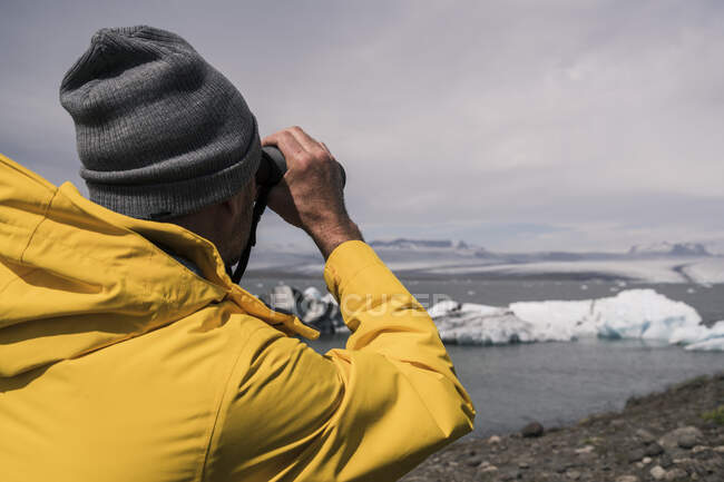 Зрелый человек смотрит ледник Ватнайокулл с биноклем, Исландия — стоковое фото
