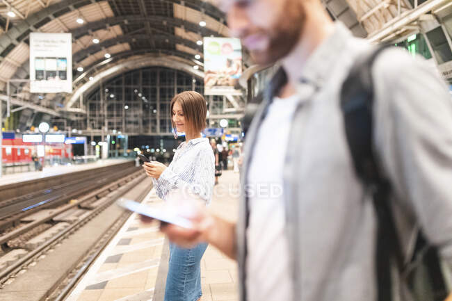 Люди, ожидающие поезда на вокзале и пользующиеся смартфонами, Берлин, Германия — стоковое фото
