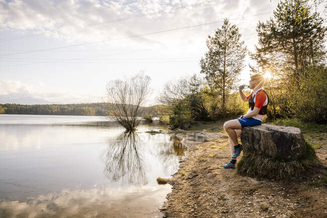 Sportive man sitting on a rock at the lakeside at sunset, Forstsee, Carinthia, Austria — Fotografia de Stock