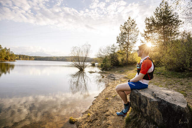 Sportive man sitting on a rock at the lakeside at sunset, Forstsee, Carinthia, Austria — Stock Photo