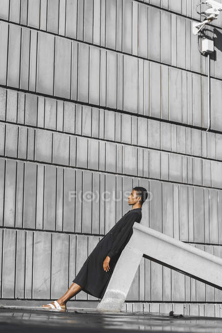 Joven vestido de negro kaftan apoyado en la estructura de hormigón al aire libre - foto de stock