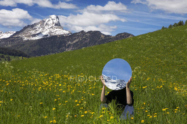 Mulher sentada no prado, escondida atrás do espelho, refletindo as montanhas de Val Badia, Alto Adige, Itália — Fotografia de Stock