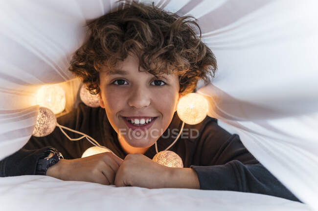 Портрет щасливого хлопця з ланцюжком світла під ліжком. — стокове фото
