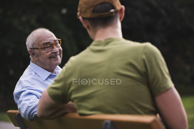 Ritratto di uomo anziano sorridente che si rilassa insieme a suo nipote su una panchina del parco — Foto stock