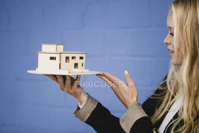 Giovane donna d'affari che tiene modello architettonico al muro blu — Foto stock