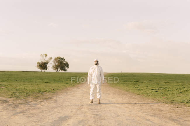 Man wearing protective suit and mask standing on dirt track in the countryside — Stock Photo