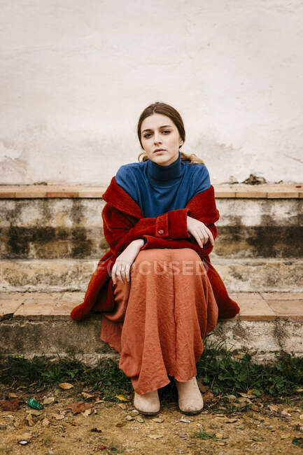 Gros plan portrait de femme avec pull col roulé bleu et manteau rouge assis sur une marche — Photo de stock