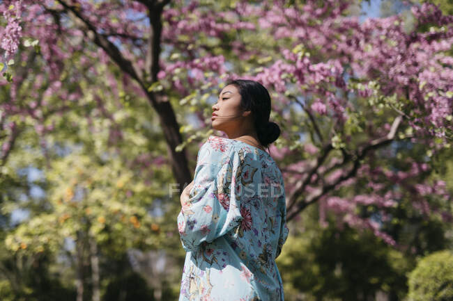 Beautiful young woman with blooming cherry tree in a public garden in spring — Stock Photo
