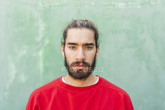 Porträt eines bärtigen jungen Mannes mit rotem Sweatshirt vor grüner Wand — Stockfoto