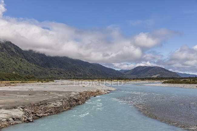 Nouvelle-Zélande, district de Westland, Whataroa, rive de la rivière Whataroa avec des montagnes boisées en arrière-plan — Photo de stock