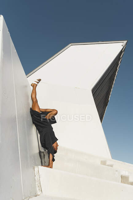 Joven vestido de negro kaftan haciendo un stand de manos al aire libre - foto de stock