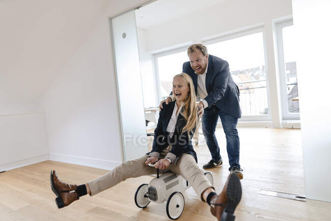 Playful businessman pushing businesswoman on toy car in office — Stock Photo
