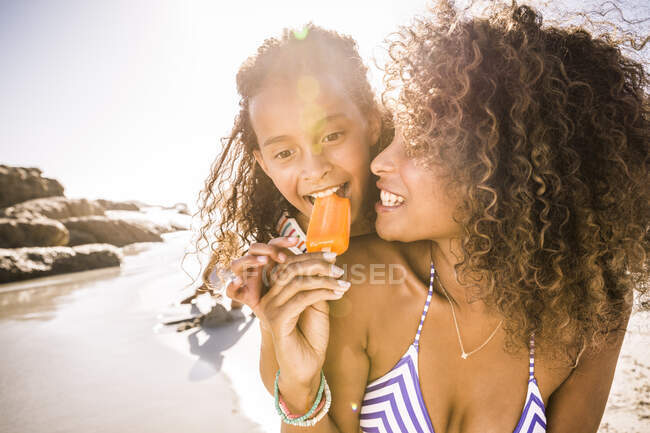 Mulher compartilhando picolé com filha na praia — Fotografia de Stock