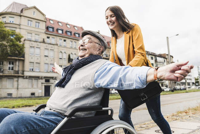 Rindo jovem mulher empurrando feliz homem sênior em cadeira de rodas — Fotografia de Stock